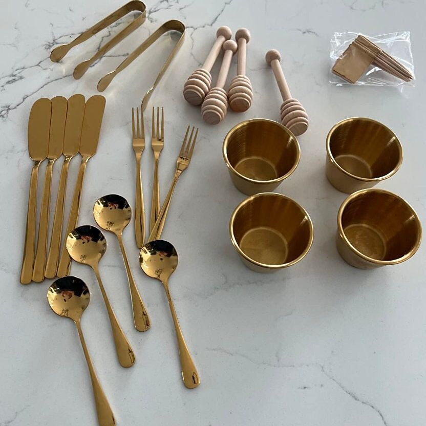 22-piece stainless steel charcuterie tool set with butter spreaders, mini bowls, and honey dippers on a wooden cheese board.