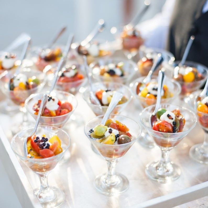 Clear acrylic appetizer cups filled with fruit, charcuterie, and small bites served at an event