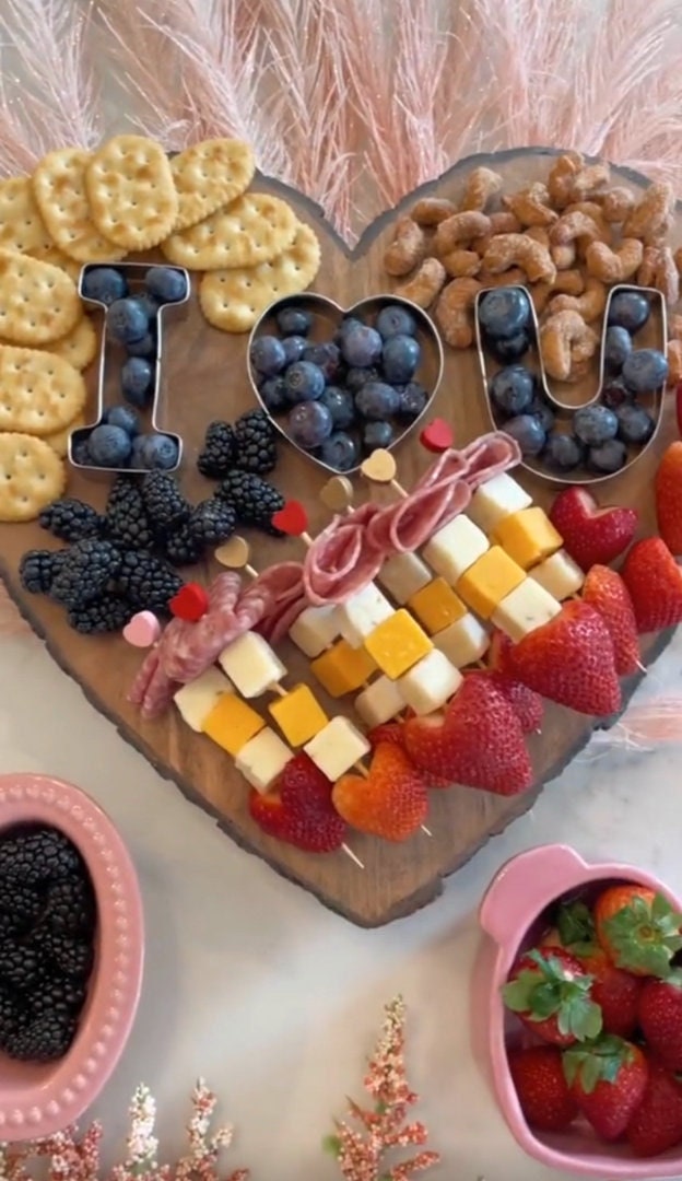 Heart-shaped bamboo board with meats, cheeses, and crackers.