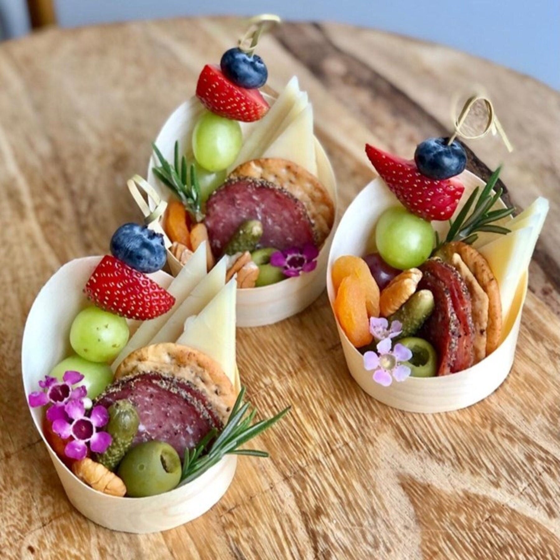 Rustic bamboo charcuterie cups with fancy toothpicks arranged on wooden table for appetizer serving