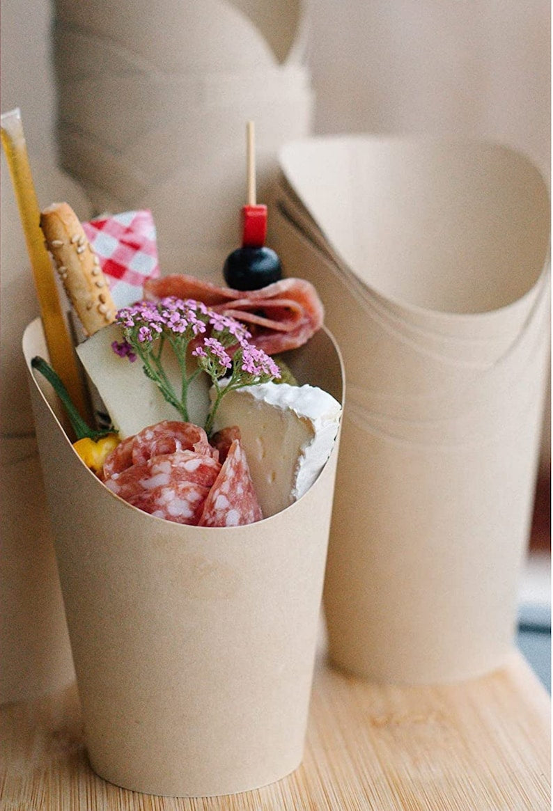 Beige charcuterie cup filled with appetizers, meats, and cheese sticks.