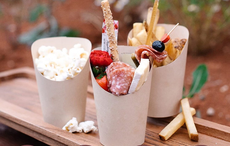 Beige charcuterie cup with popcorn and snacks for outdoor event.
