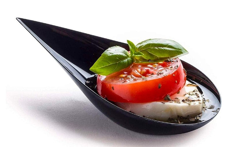 Black tasting spoon with caprese salad and basil.
