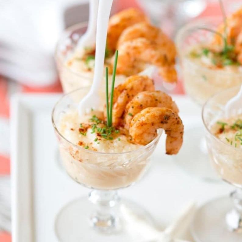 Clear mini plastic martini cups filled with shrimp cocktail appetizers and white mini forks for elegant party serving.
