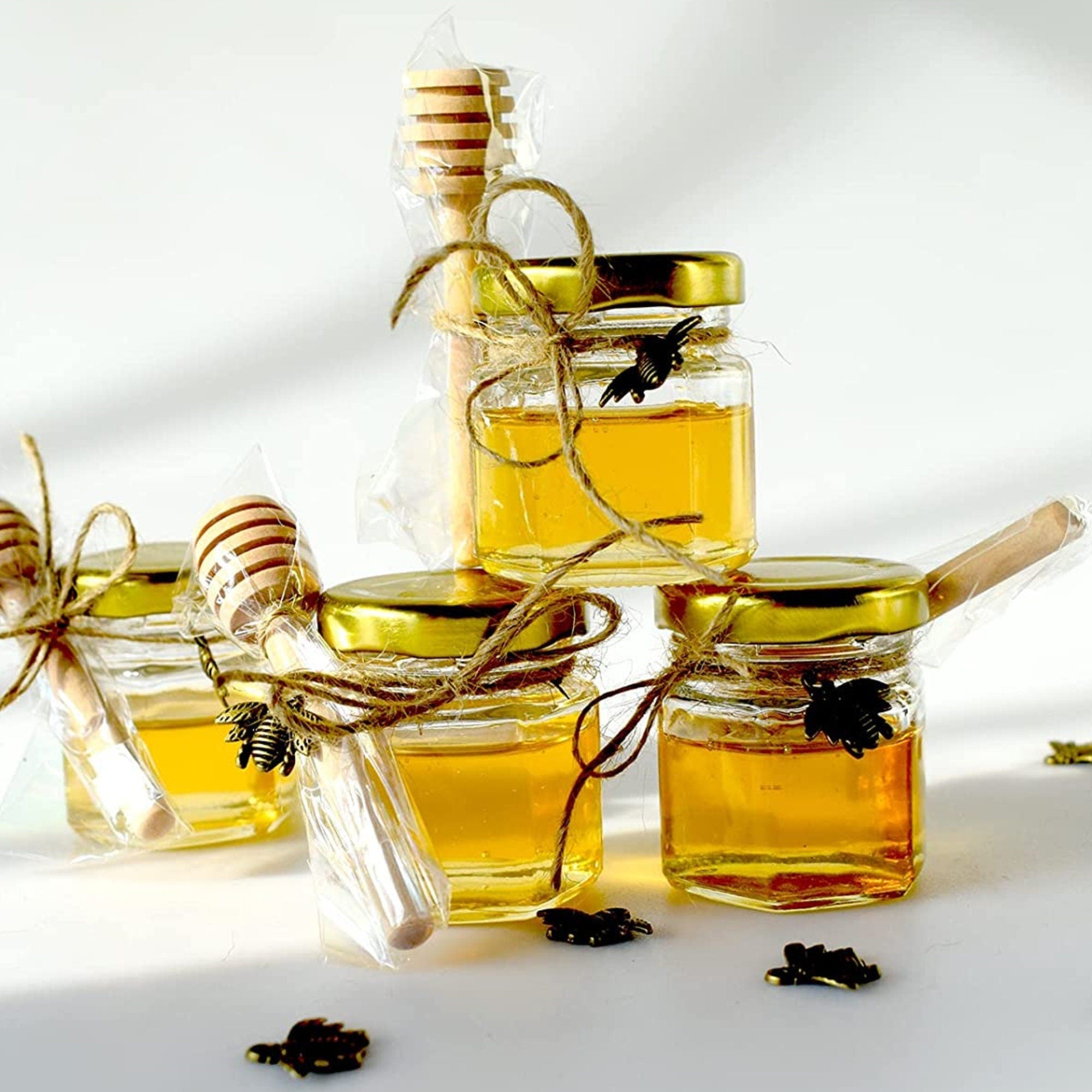 Close-up of a wooden honey dipper dipping into a mini jar of honey.