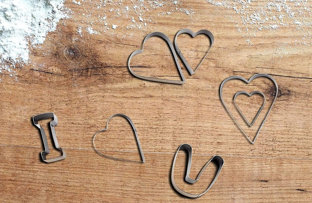 Heart-shaped cookie cutters cutting dough on a countertop.