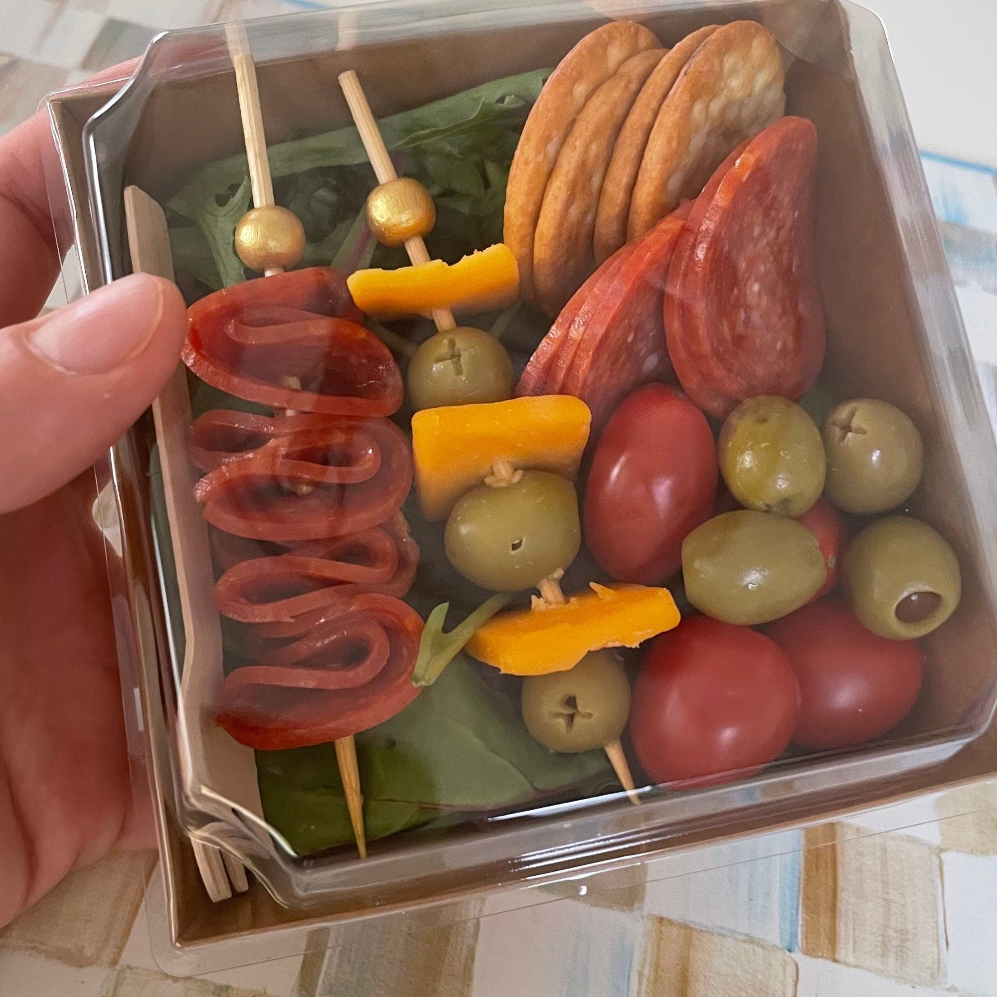 Clear lid charcuterie box filled with skewered olives and appetizers for party events