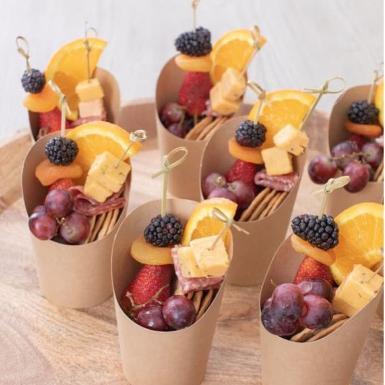 Eco-friendly kraft paper charcuterie cup with nuts, berries, and a wooden toothpick.