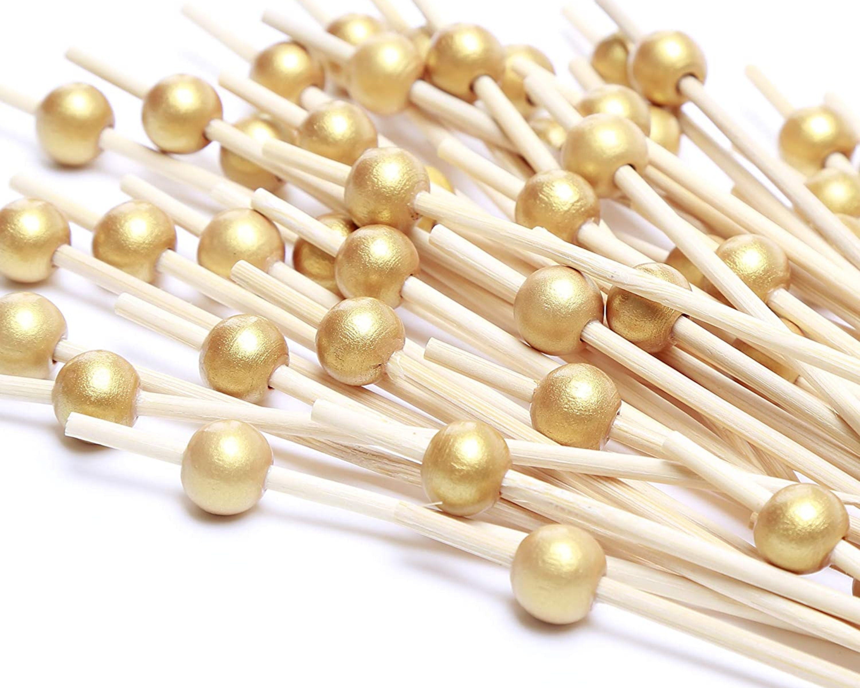 Flat lay arrangement of premium gold fancy toothpicks with shiny gold beads for upscale appetizer and charcuterie displays.