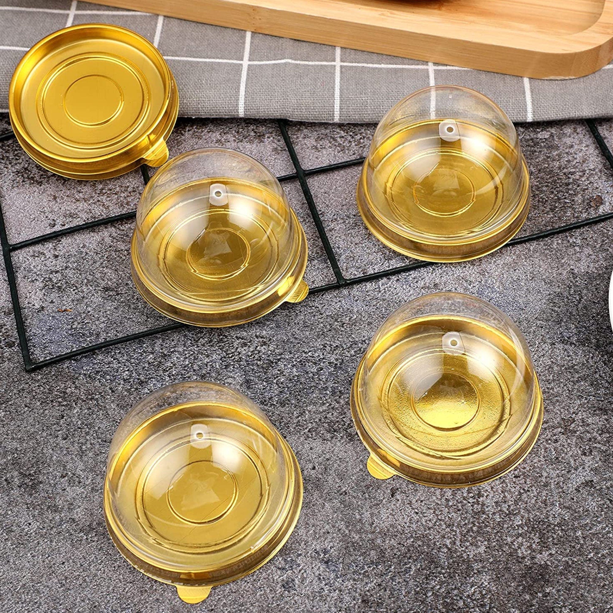 Gold bases with dome and square covers displayed on a rack, showcasing elegant clear favor boxes.