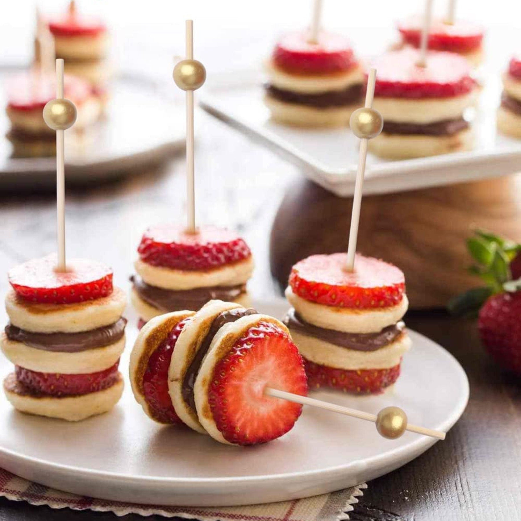 Green charcuterie cups and fancy toothpicks with mini desserts on a party table.