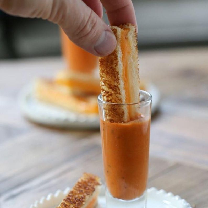 Hand dipping a slice of toast into soup served in a mini acrylic cup, showcasing the cup's functionality and upscale design for elegant dining.