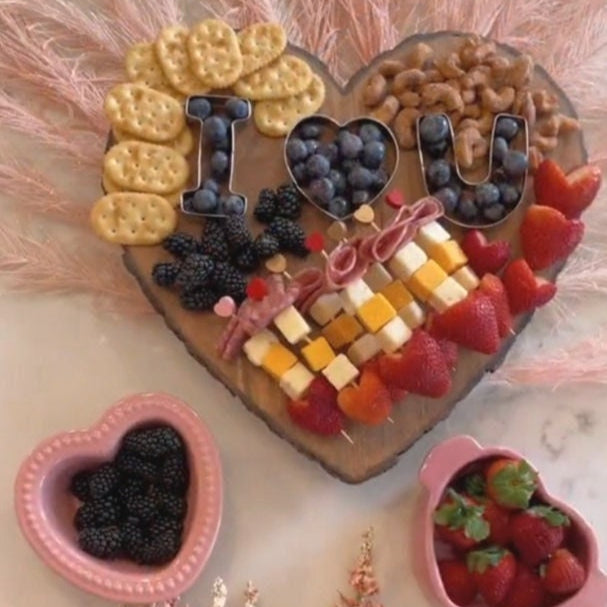 Heart-shaped bamboo charcuterie board with cheese and fruit.