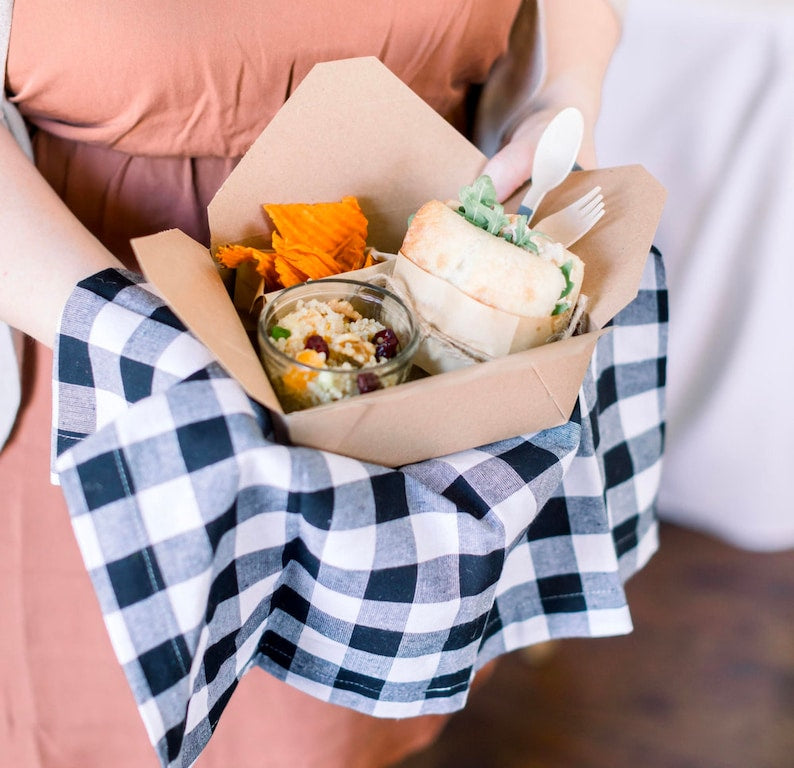 Brown kraft paper food box containing fresh wraps, artisan crackers, and creamy dip for party catering.