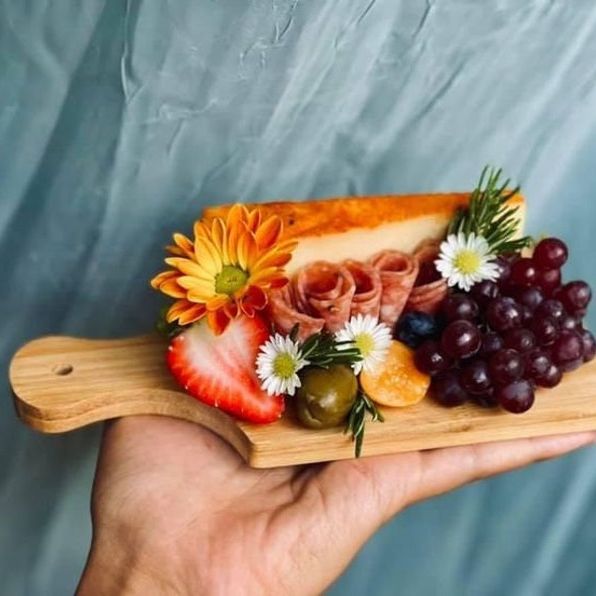 Hand presenting mini charcuterie board with meats, fruit, and herbs
