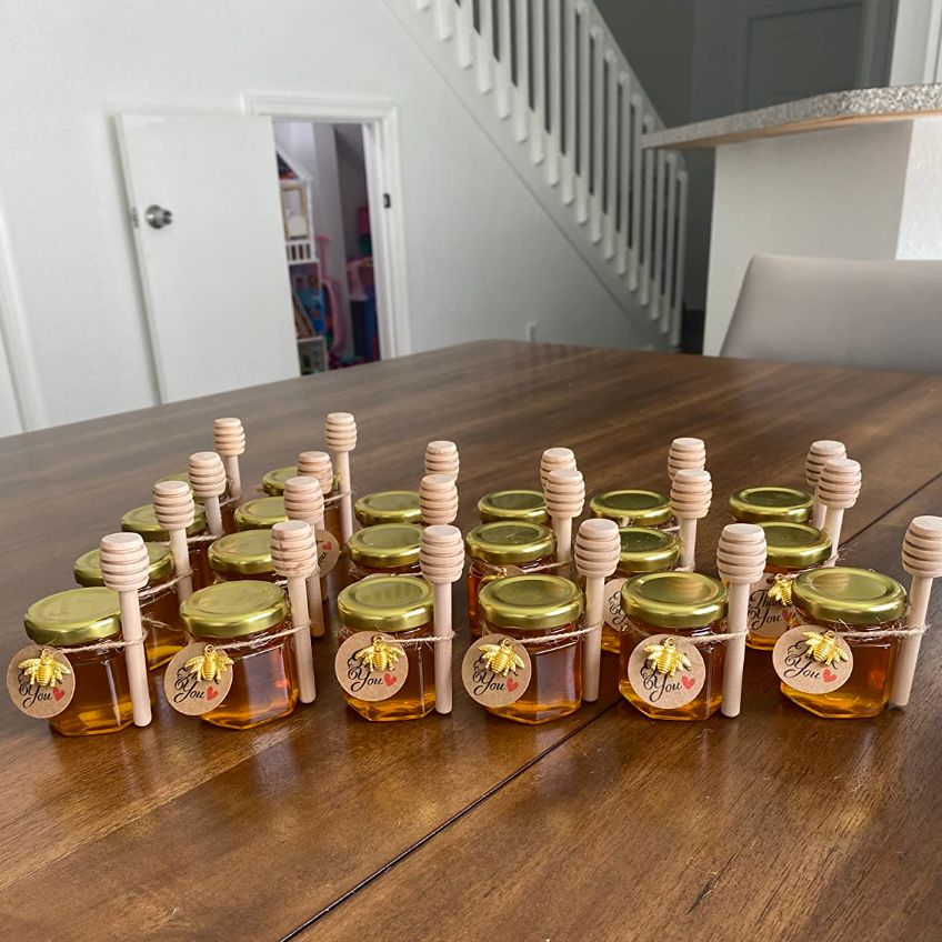 Group of mini honey jars with wooden dippers on a table.
