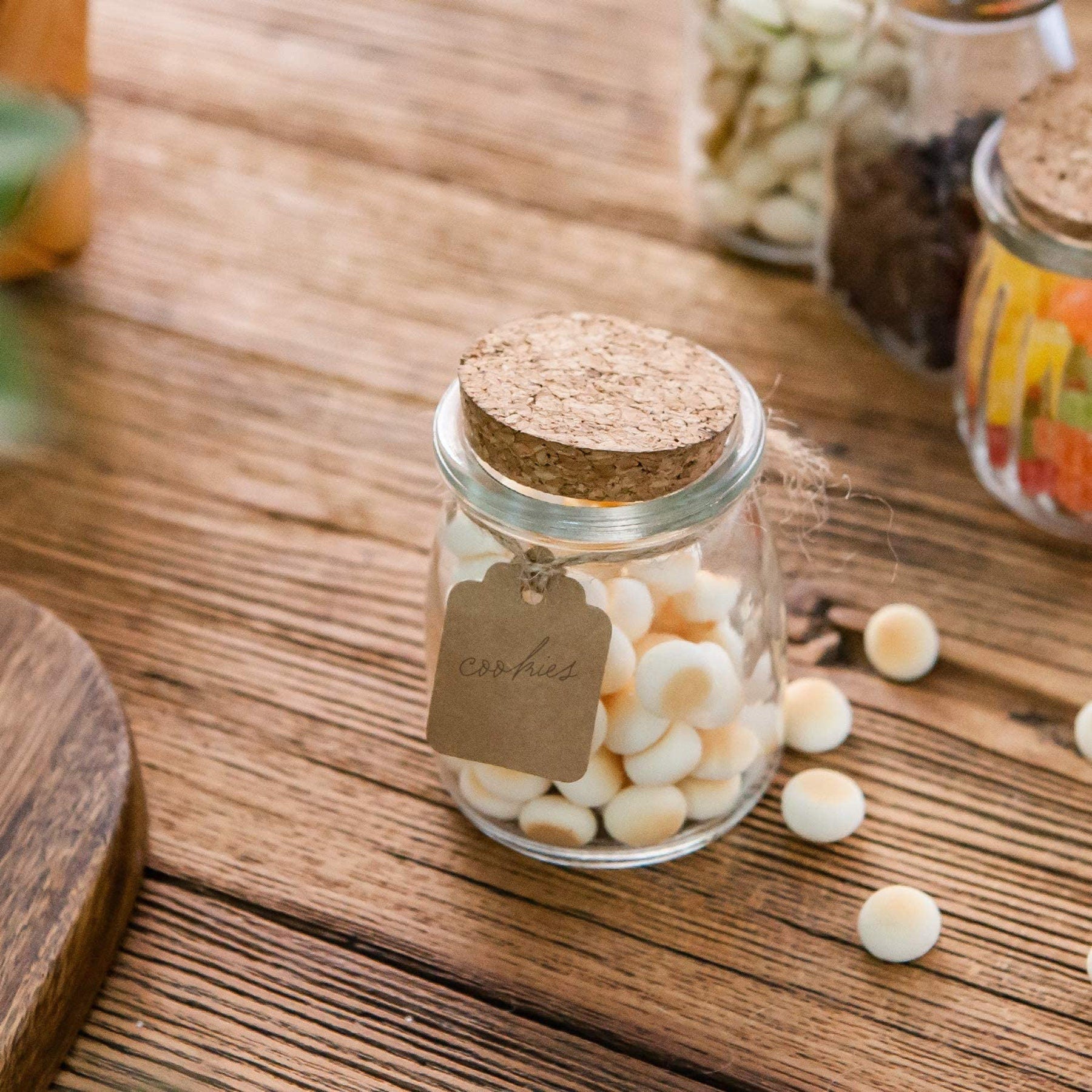 Hand holding mini glass jar with cork lid next to party spread