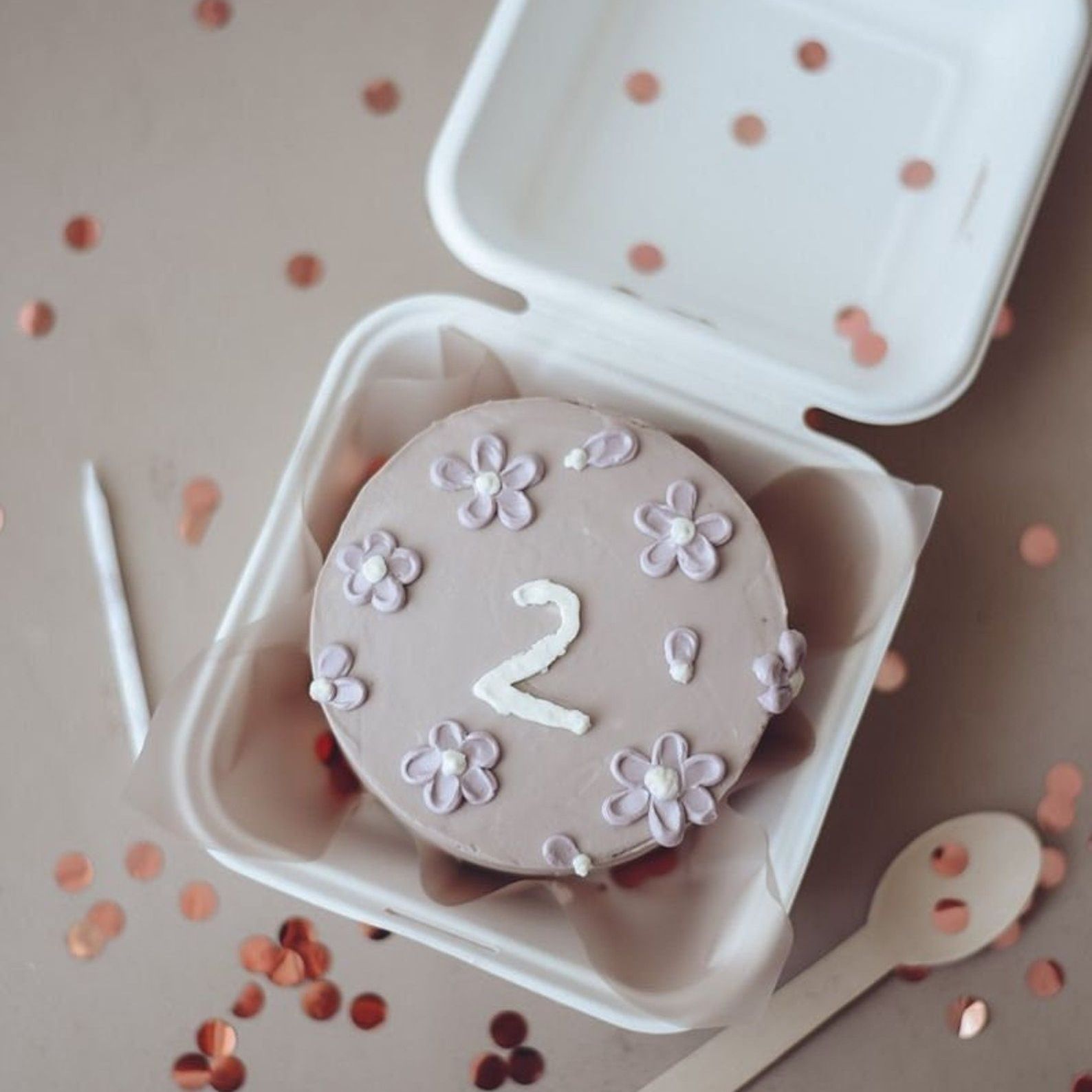 Pink floral cake displayed in a kraft cake gift box with a wooden spoon beside it.