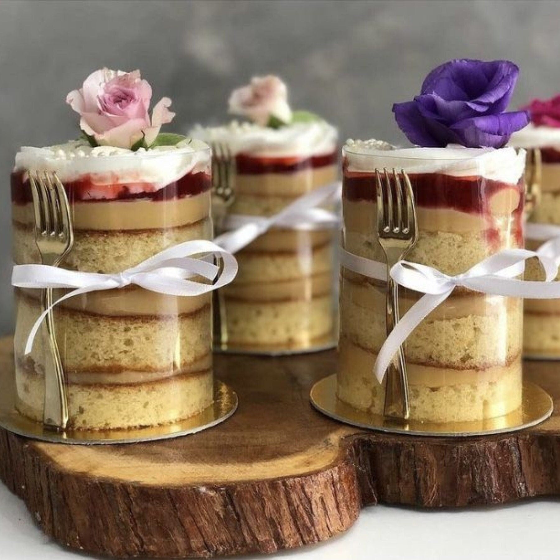 Silver mini fork placed next to a wrapped cake with a transparent plastic cake wrap on a sturdy gold board.