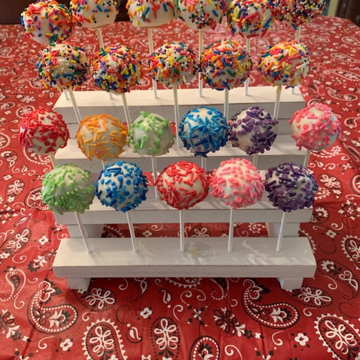 3 tier wooden cake pop stand holding colorful cake pops.