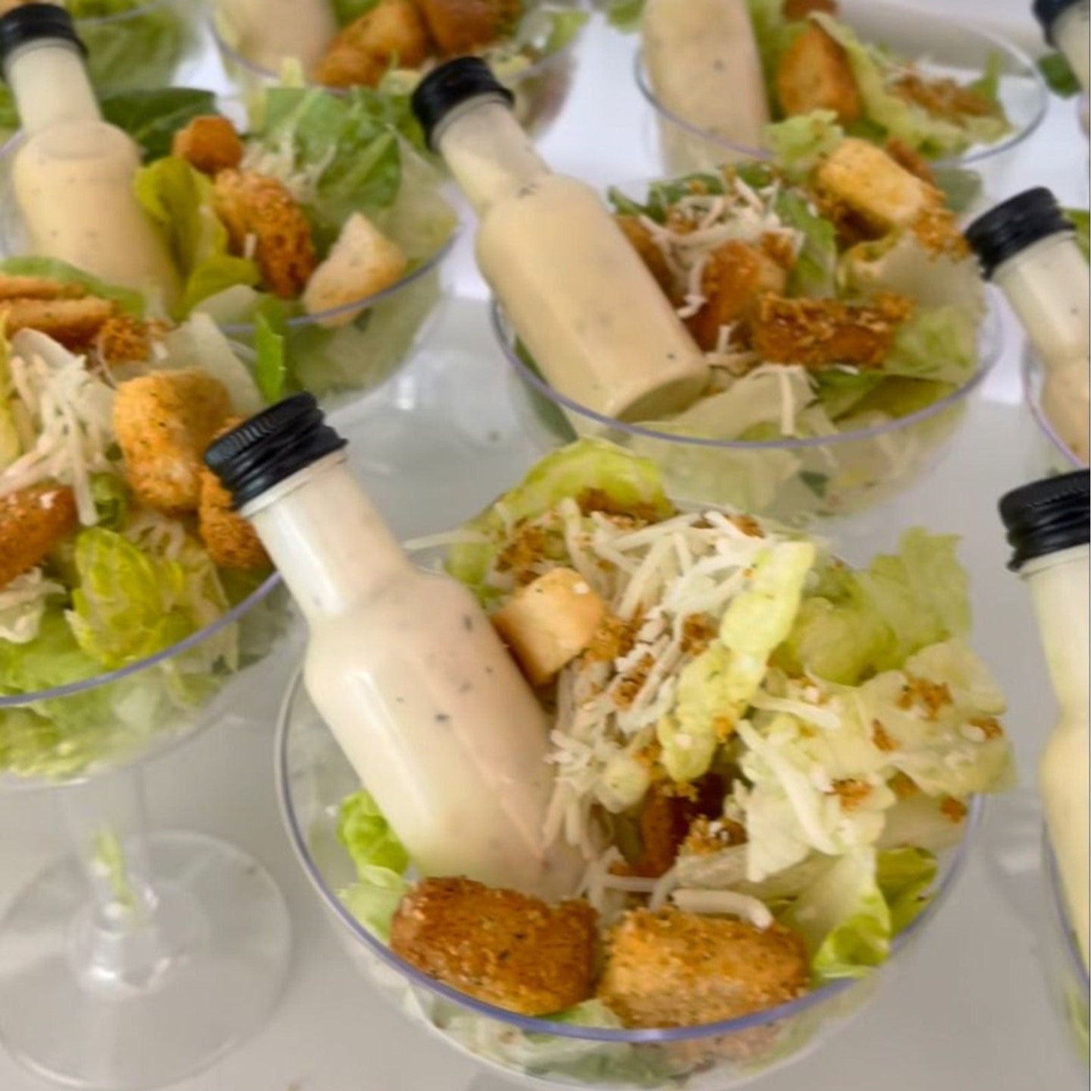 Clear acrylic salad cups with 4oz or 8oz options, mini dressing bottles, and forks on an elegant table setting for a party.