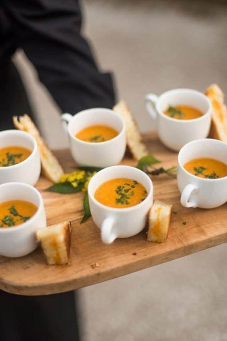 White plastic soup mugs with tomato bisque served on tray
