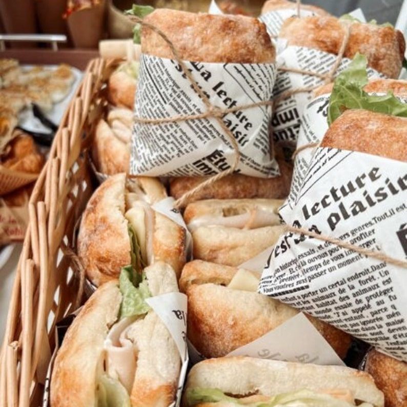 Basket filled with sandwiches wrapped in rustic newspaper-style sandwich paper for vintage food presentation and catering.