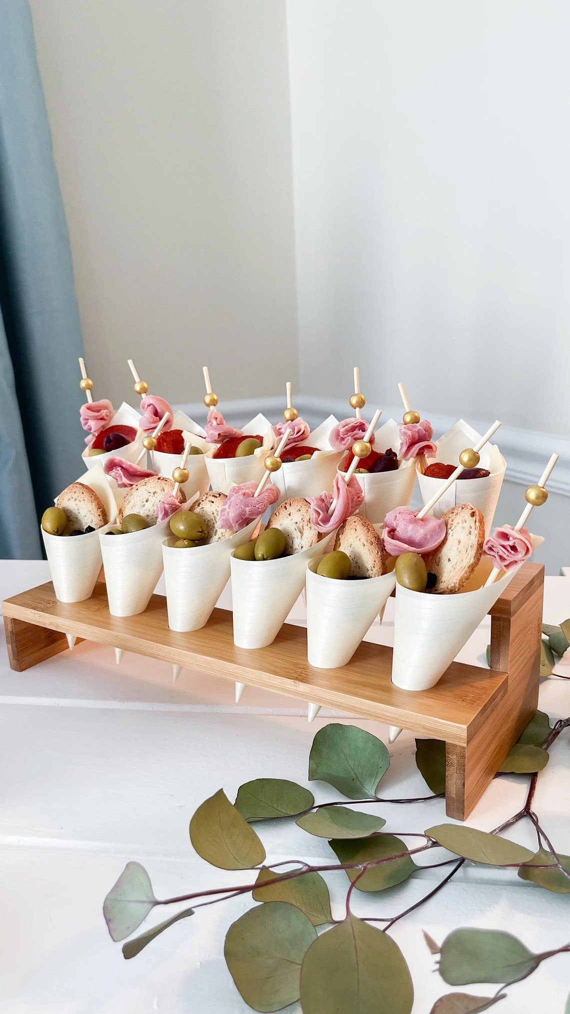 Single-serving charcuterie cups on a tiered bamboo stand. Wooden appetizer cones for a wedding or party.
