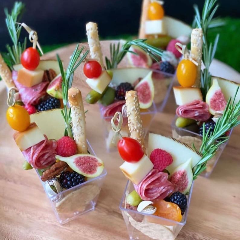 Party serving cups with cheese, crackers, and fruit on display