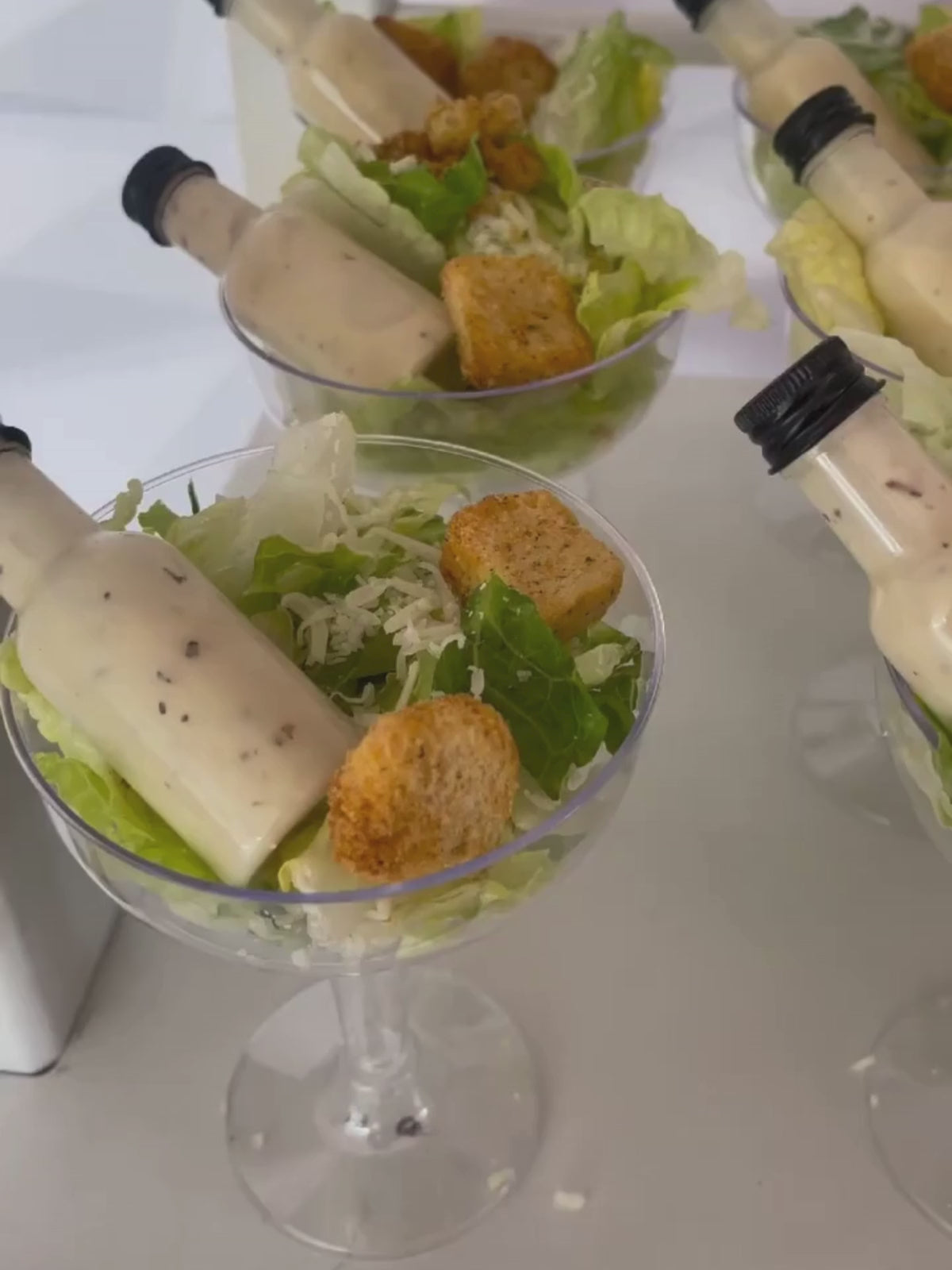 Clear acrylic salad cups with 4oz or 8oz options, mini dressing bottles, and forks on an elegant table setting for a party.