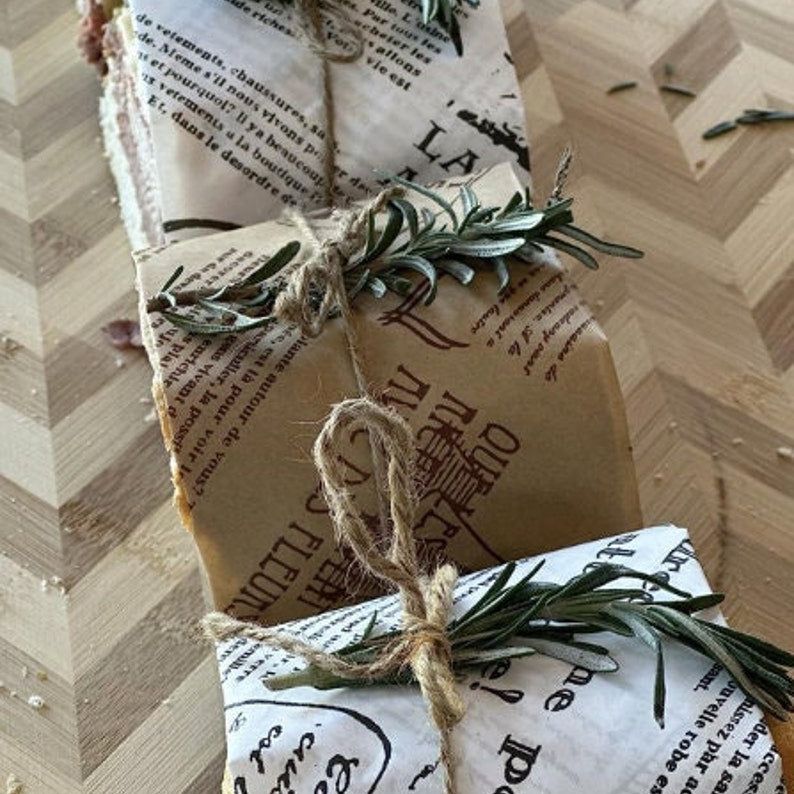 Sandwiches wrapped in newspaper deli sheets tied with twine and fresh rosemary garnish for elegant rustic food presentation.
