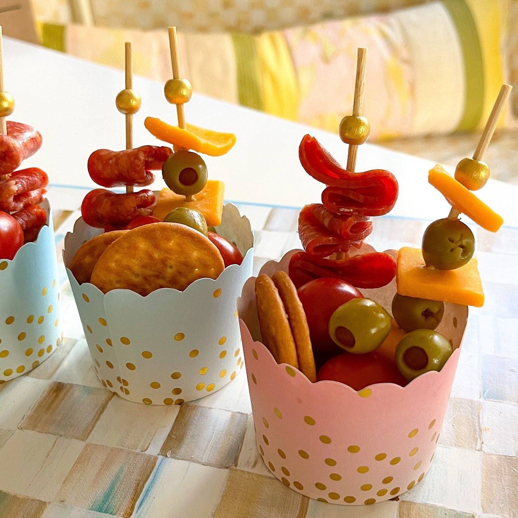 Scalloped charcuterie cups with crackers, olives, and cheese displayed with fancy gold toothpicks – perfect appetizer serving cups.