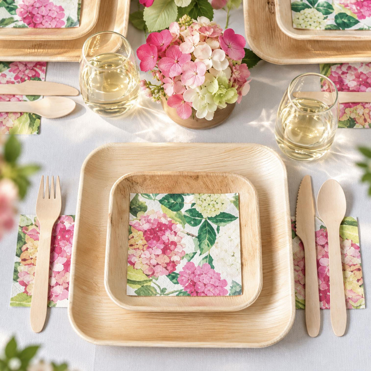 Table setting with square palm leaf plates and matching disposable wooden fork, knife, and spoon for a party.