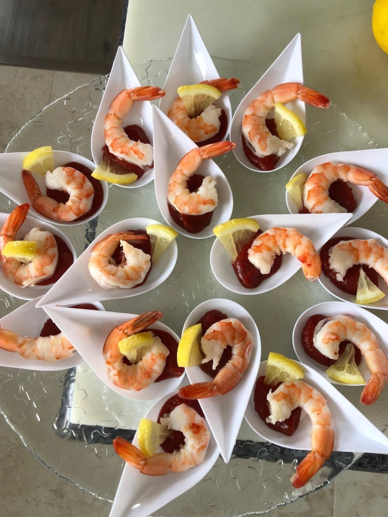 Shrimp cocktail bites arranged in white Asian spoons for a catered appetizer tray.