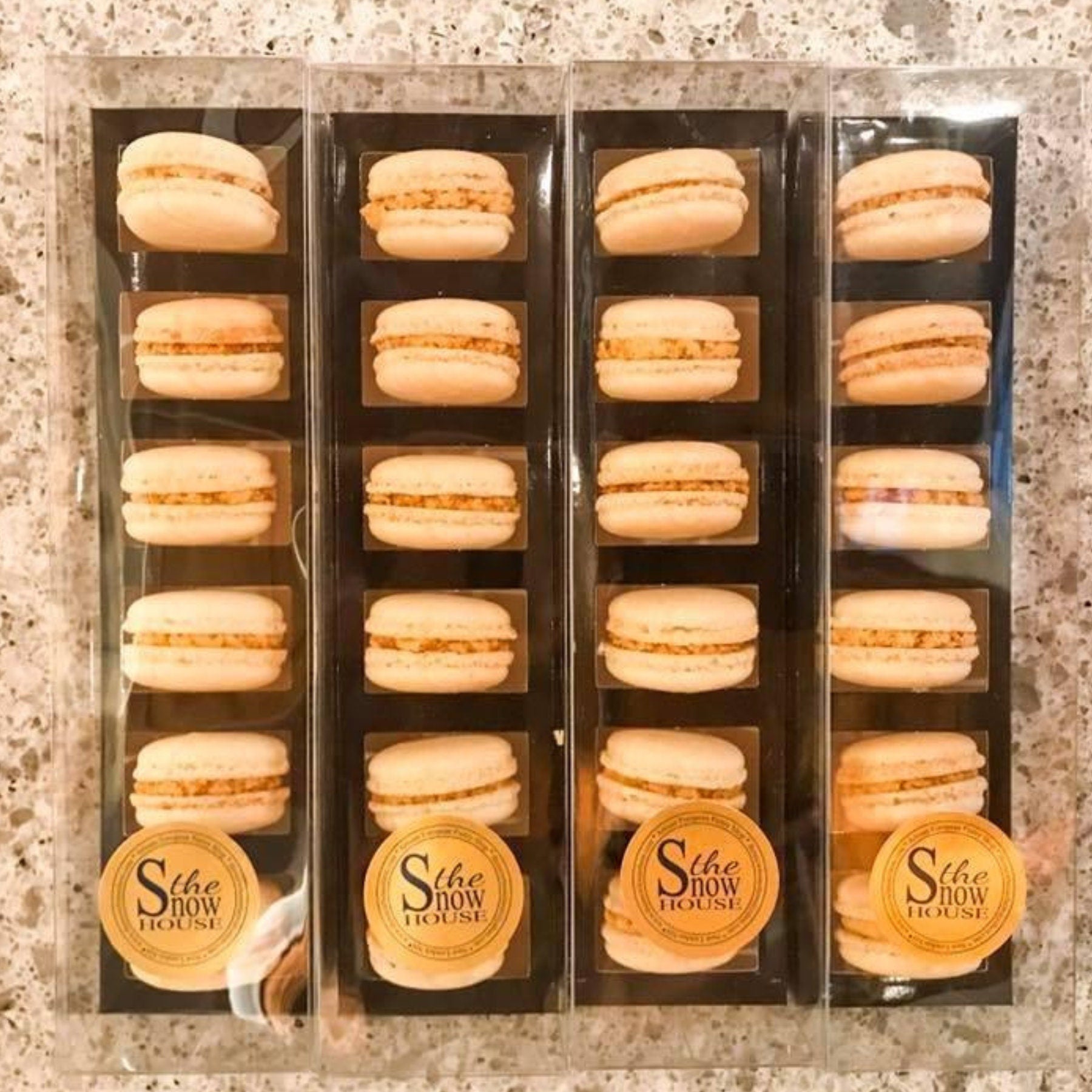 Vertical stack of black macaroon boxes loaded with tan macarons for bakery display