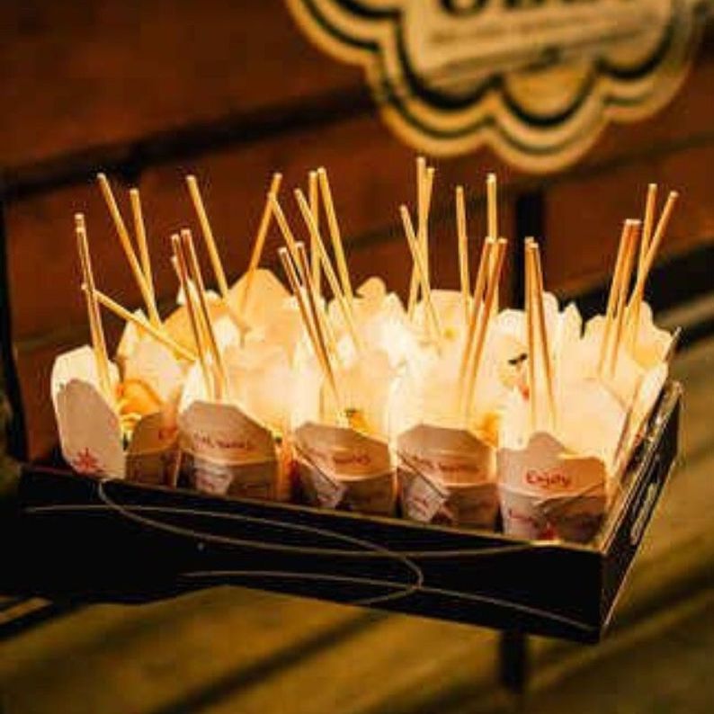 Buffet station serving noodles in white Chinese take out boxes with disposable wooden chopsticks.