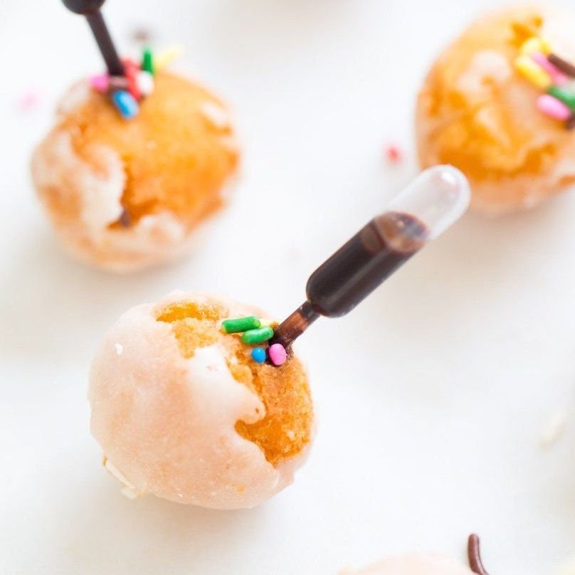 Bite-size cake pops topped with round and long pipettes filled with sauce