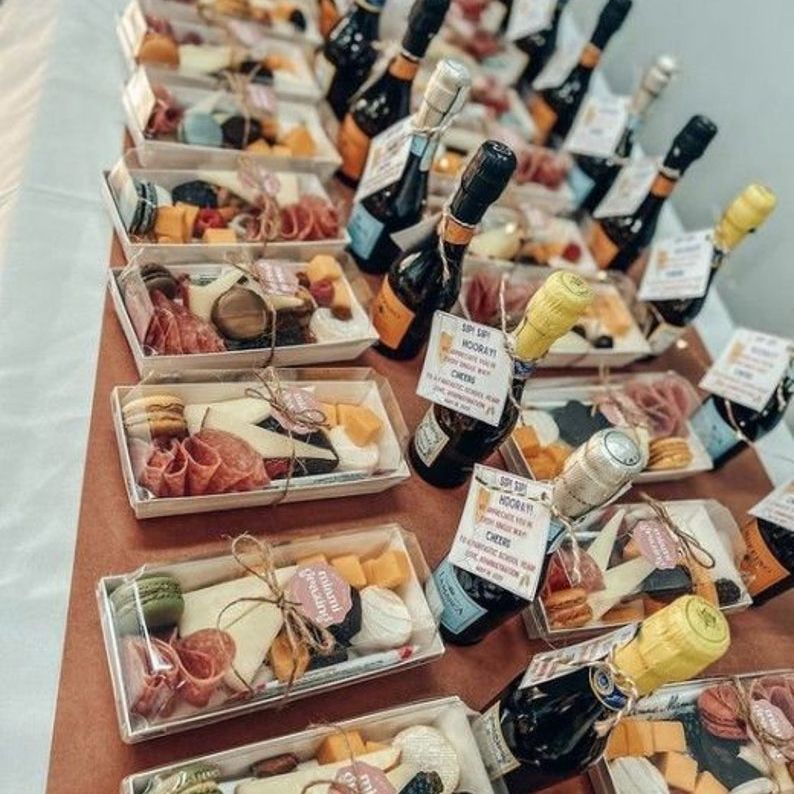 Individual charcuterie boxes displayed with champagne bottles at a party.