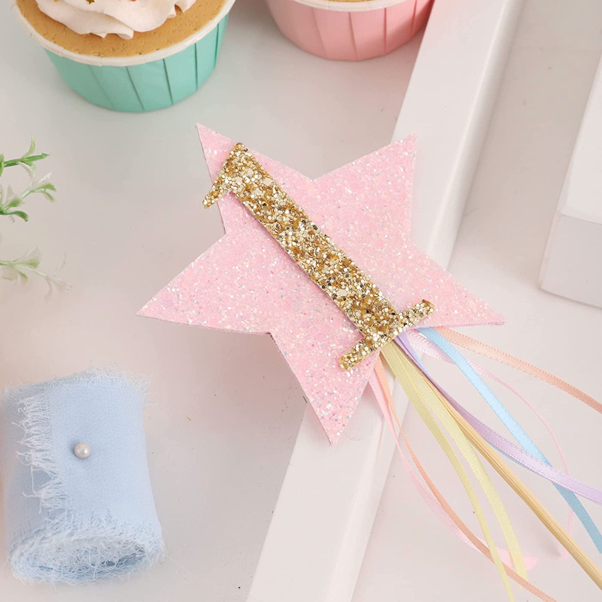 Close-up of glitter cake topper on white and pink decorated first birthday celebration cake
