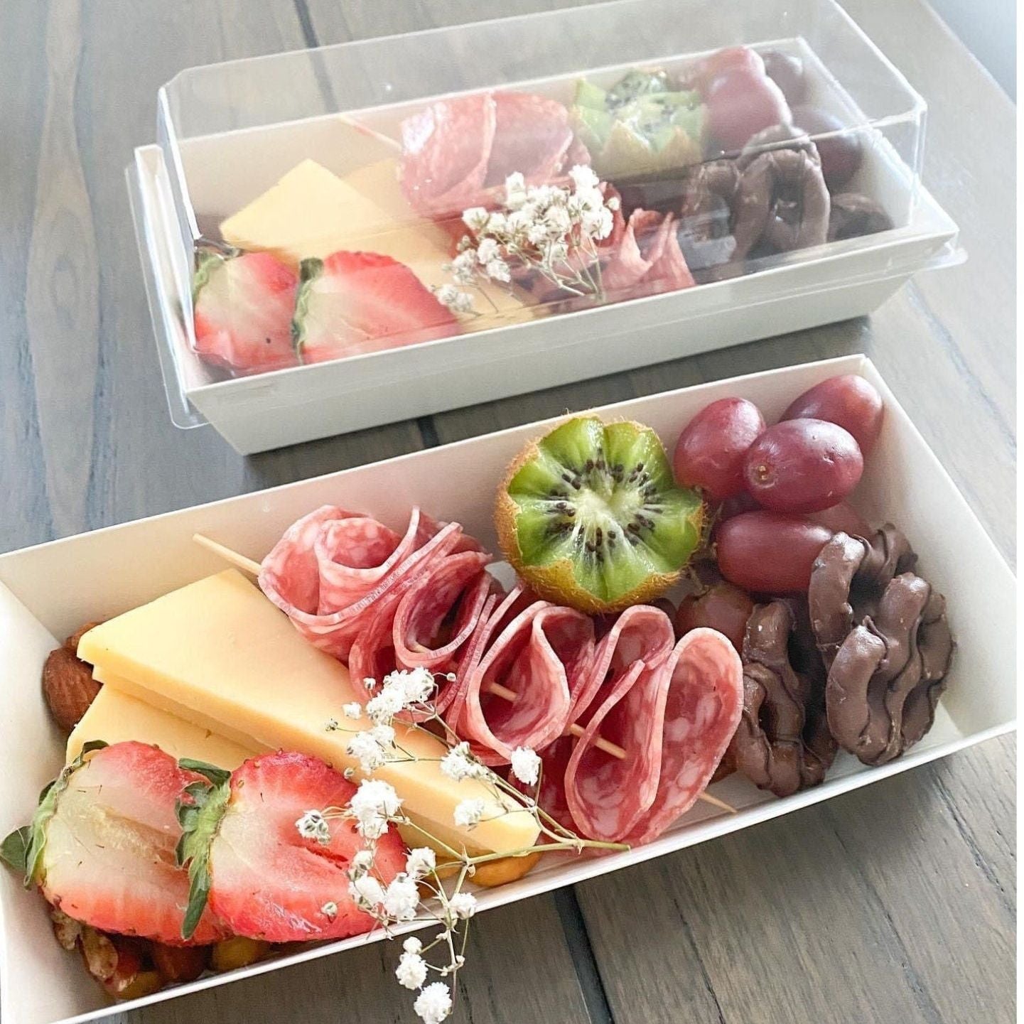 Individual charcuterie box with clear lid filled with cheese, meats, fruit, and strawberries.