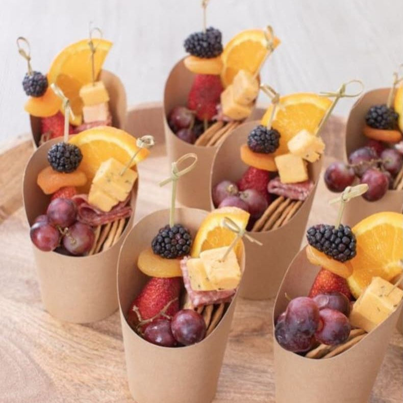 Eco-friendly kraft paper charcuterie cup with nuts, berries, and a wooden toothpick.