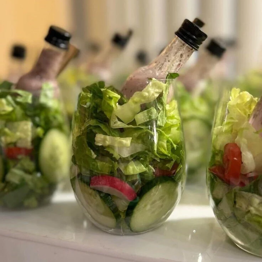 Individual salad cups with dressing bottles and mini forks artfully displayed on a catering table.