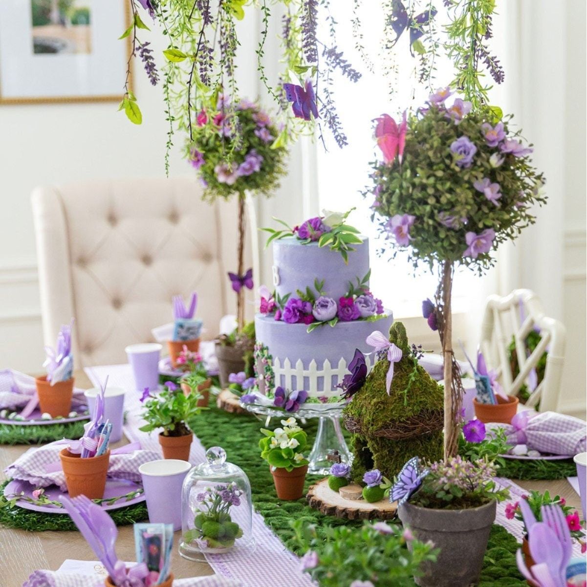 Fairy-themed party table decorated with faux grass runner, flowers, and hanging plants