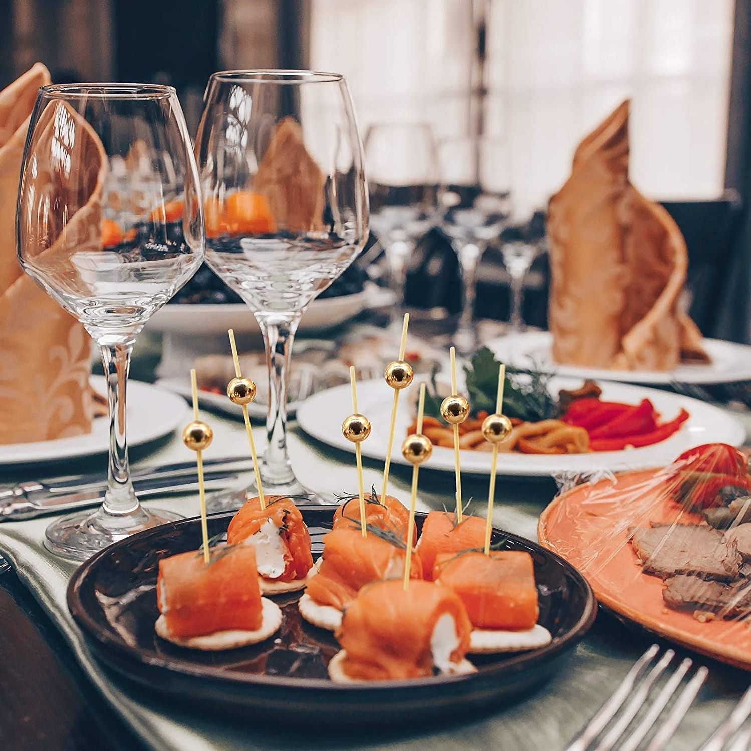 Fancy toothpicks with gold beads at an elegant dinner party setting for sophisticated appetizers.