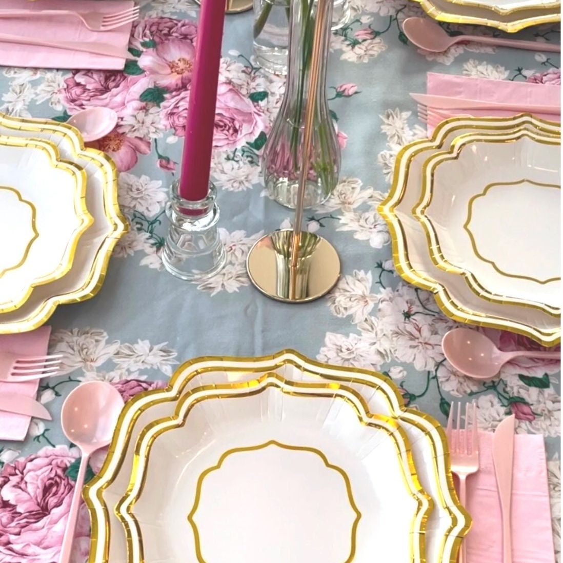 Close-up of layered pink and gold scalloped plates on a floral tablecloth with pink candles