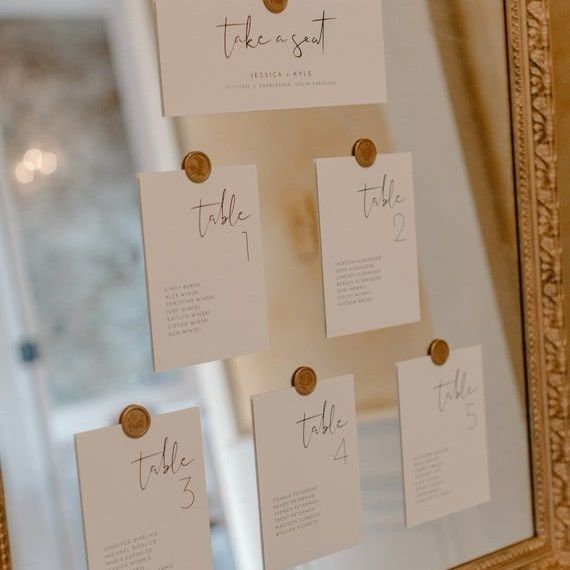 Gold frame display of escort cards secured with matching 1-inch wax seal stickers for a wedding seating chart.