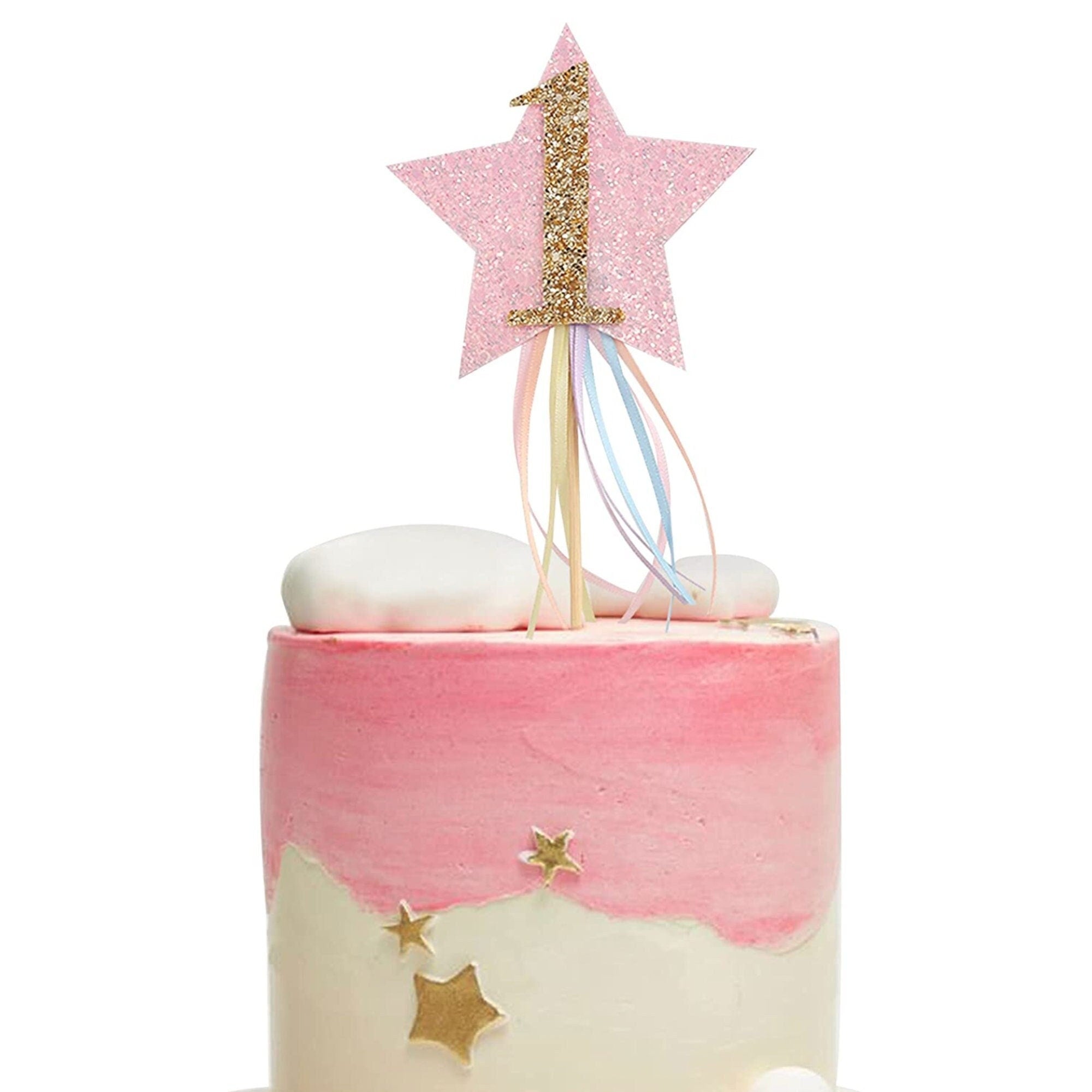 Gold star first birthday cake topper with number 1 and pastel ribbons on pink frosted cake