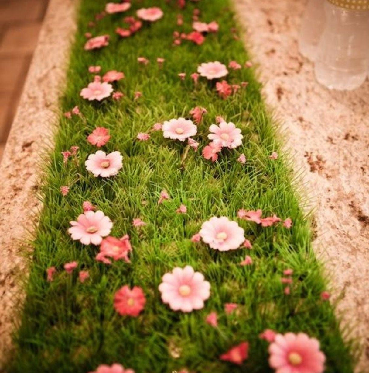 Artificial turf table runner decorated with pink daisy flowers for a fairy-themed event
