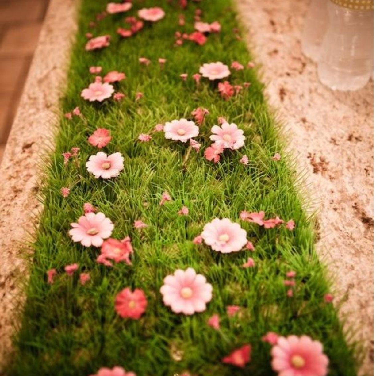 Artificial turf table runner decorated with pink daisy flowers for a fairy-themed event