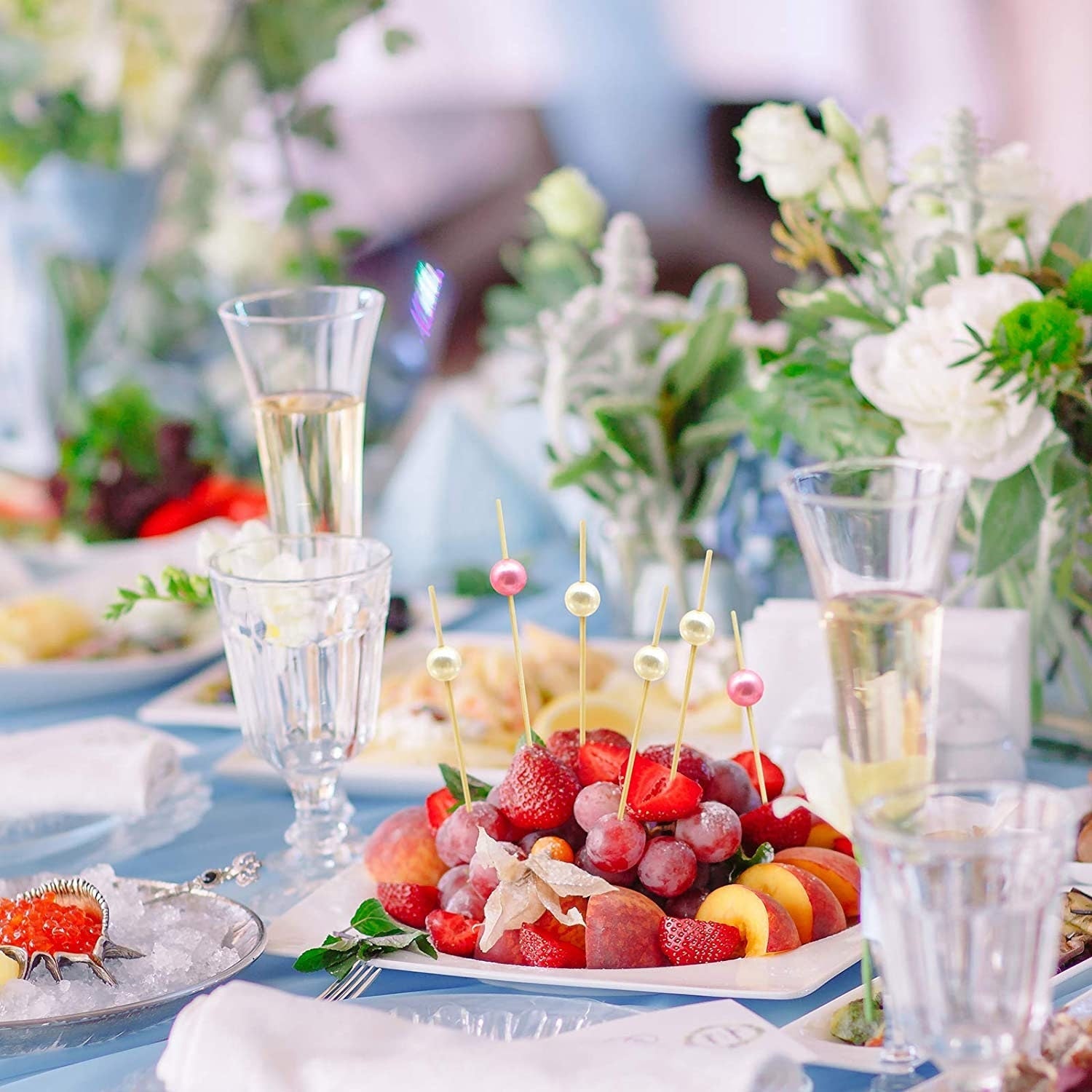 Grazing table setup featuring assorted bead fancy toothpicks in colorful fruits and desserts for elegant party presentation.